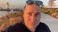 a bald man is taking a selfie in front of a lighthouse